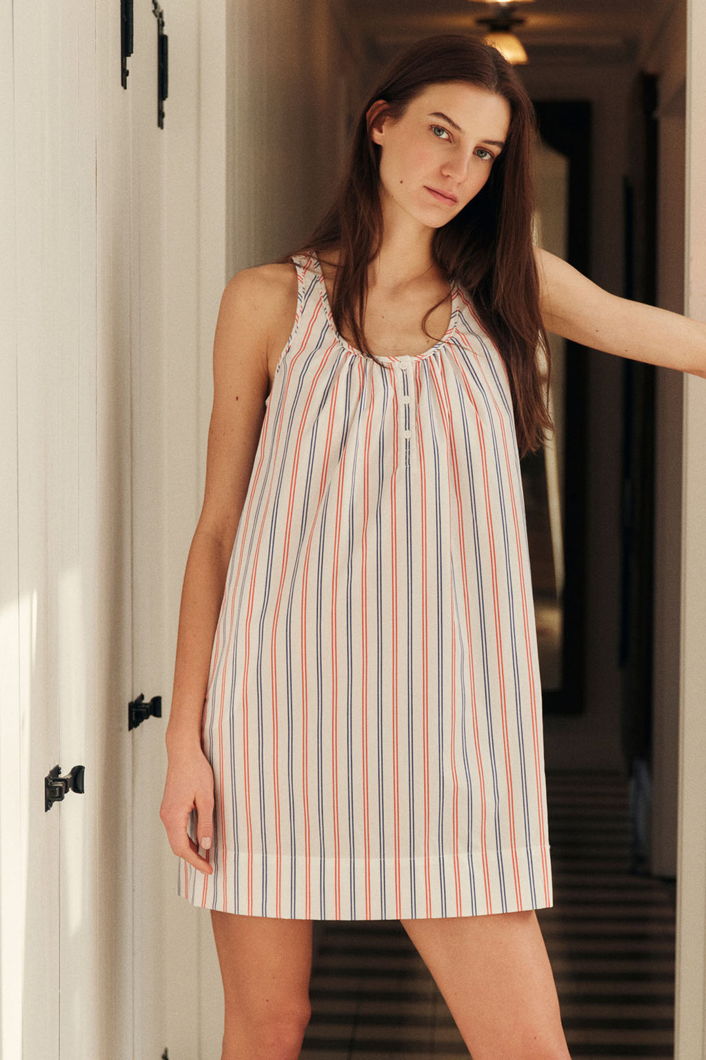 Woman wearing sleeveless nightgown with vertical red and blue stripes on white background.