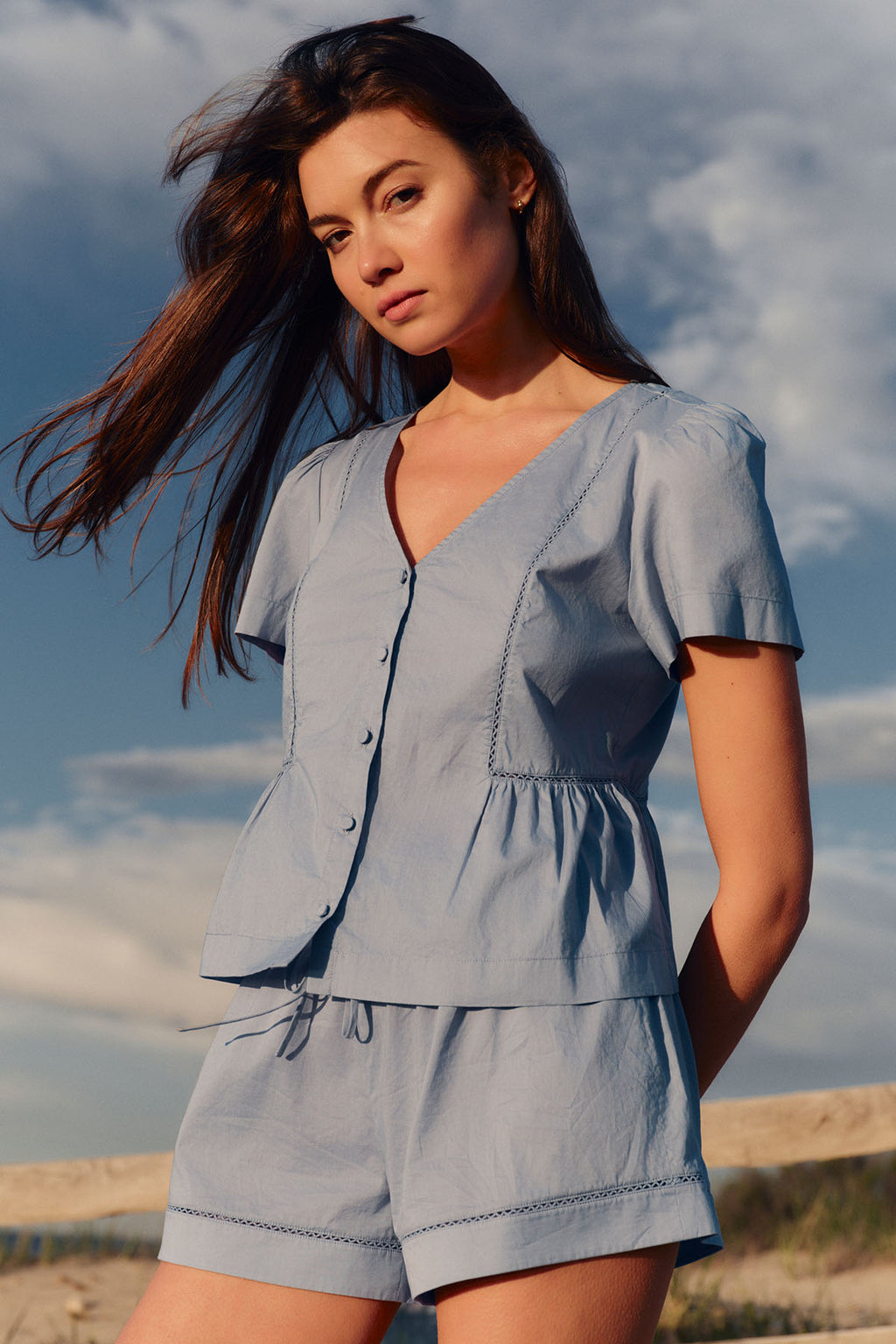 Woman wearing a dusty blue two-piece set with button-front top and matching shorts with drawstring waist.