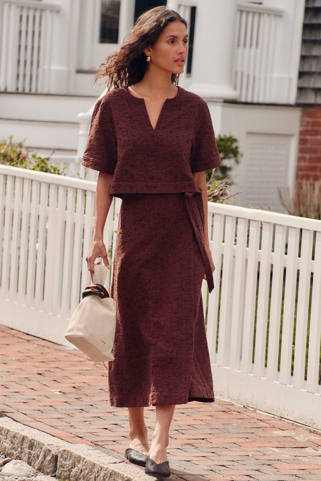 Woman wearing a cocoa brown jacquard popover top and matching midi skirt with a v-neckline and tie waist.