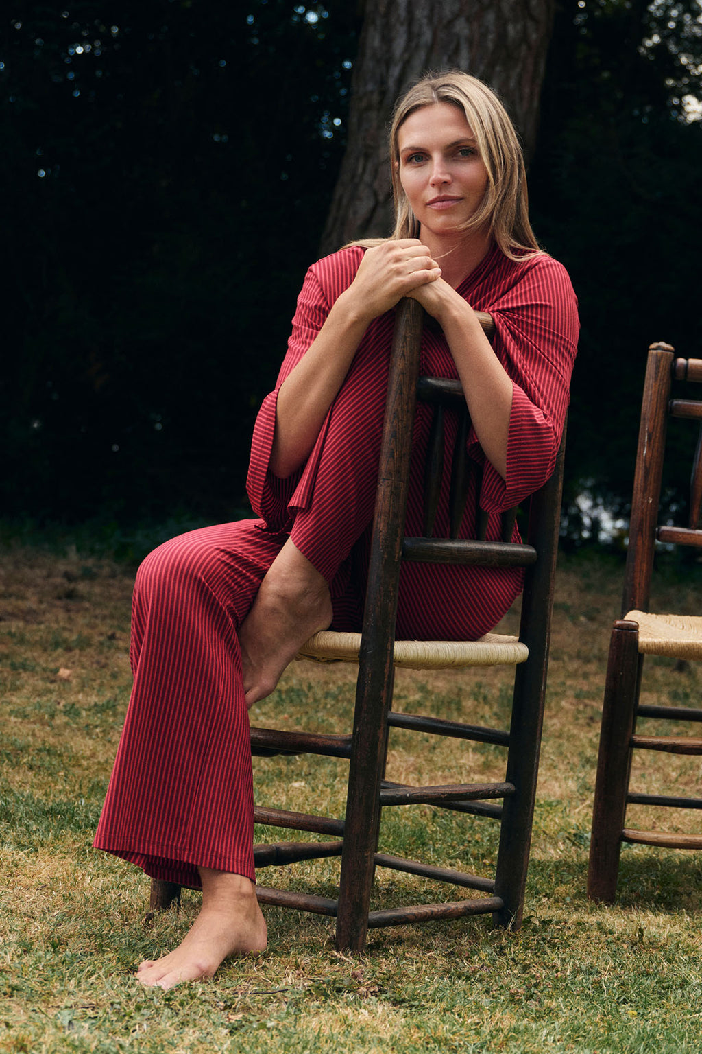 Woman wearing burgundy pencil-striped kimono robe and matching pants, seated outdoors.