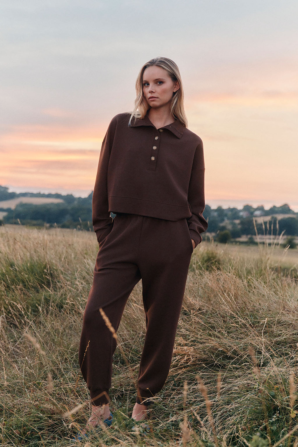 Woman wearing dark brown pullover with polo collar and matching jogger pants standing in a field.