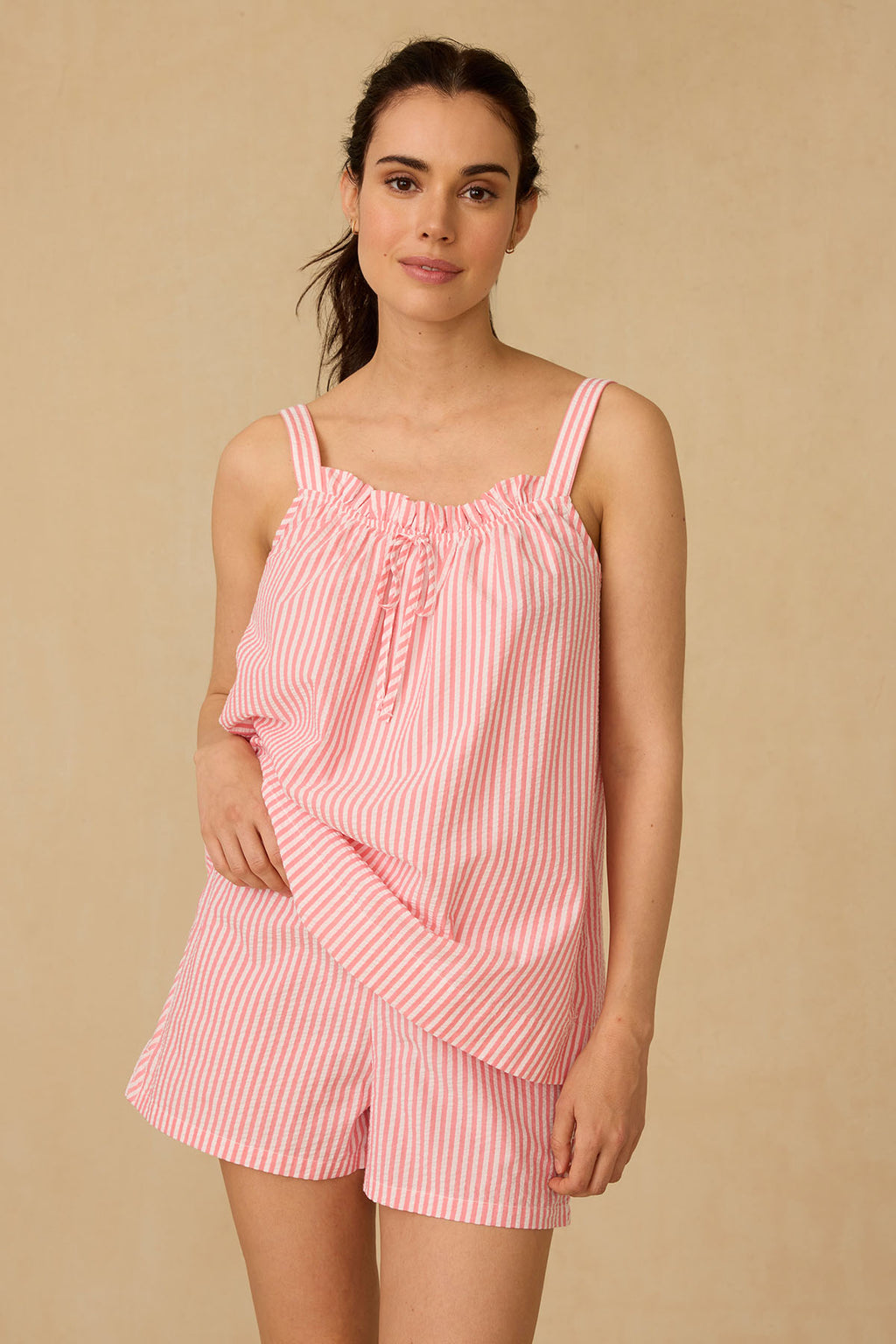 A woman wearing the Alice Shorts Set in Gelato Seersucker stands against a plain beige background, smiling gently with one hand on her hip.