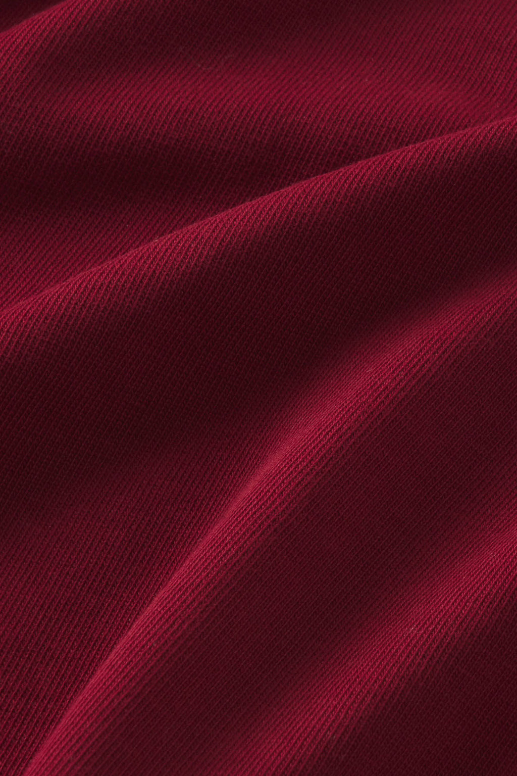 Deep burgundy ribbed fabric with diagonal fold details and textured surface.