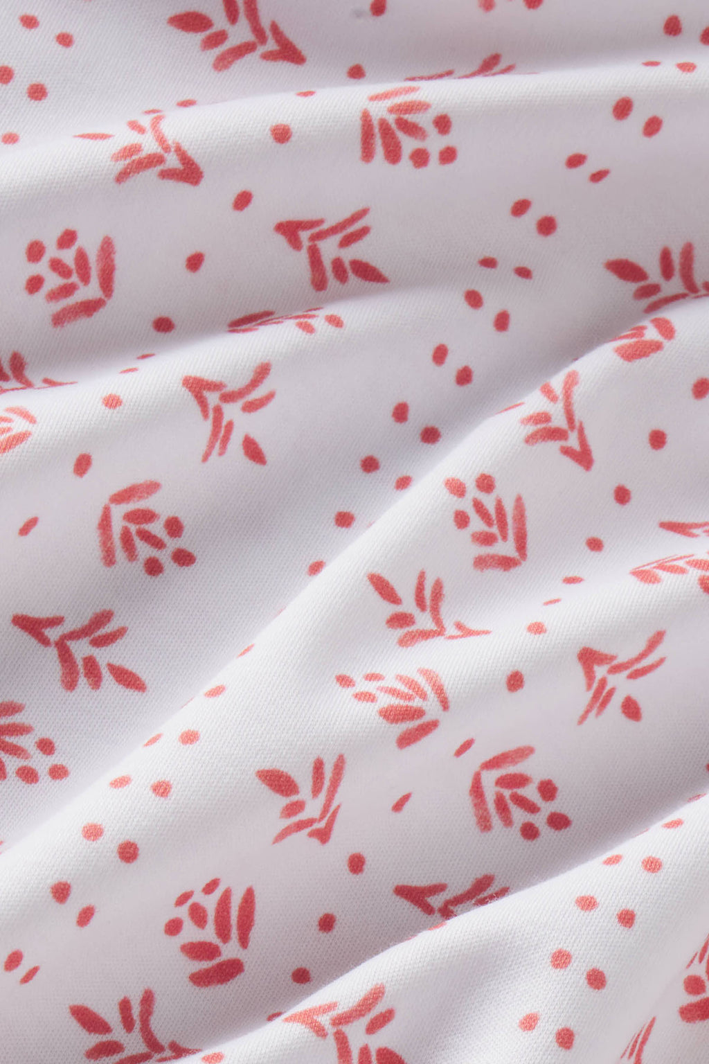 White Pima cotton fabric with red leaf and dot pattern showing gathered folds.