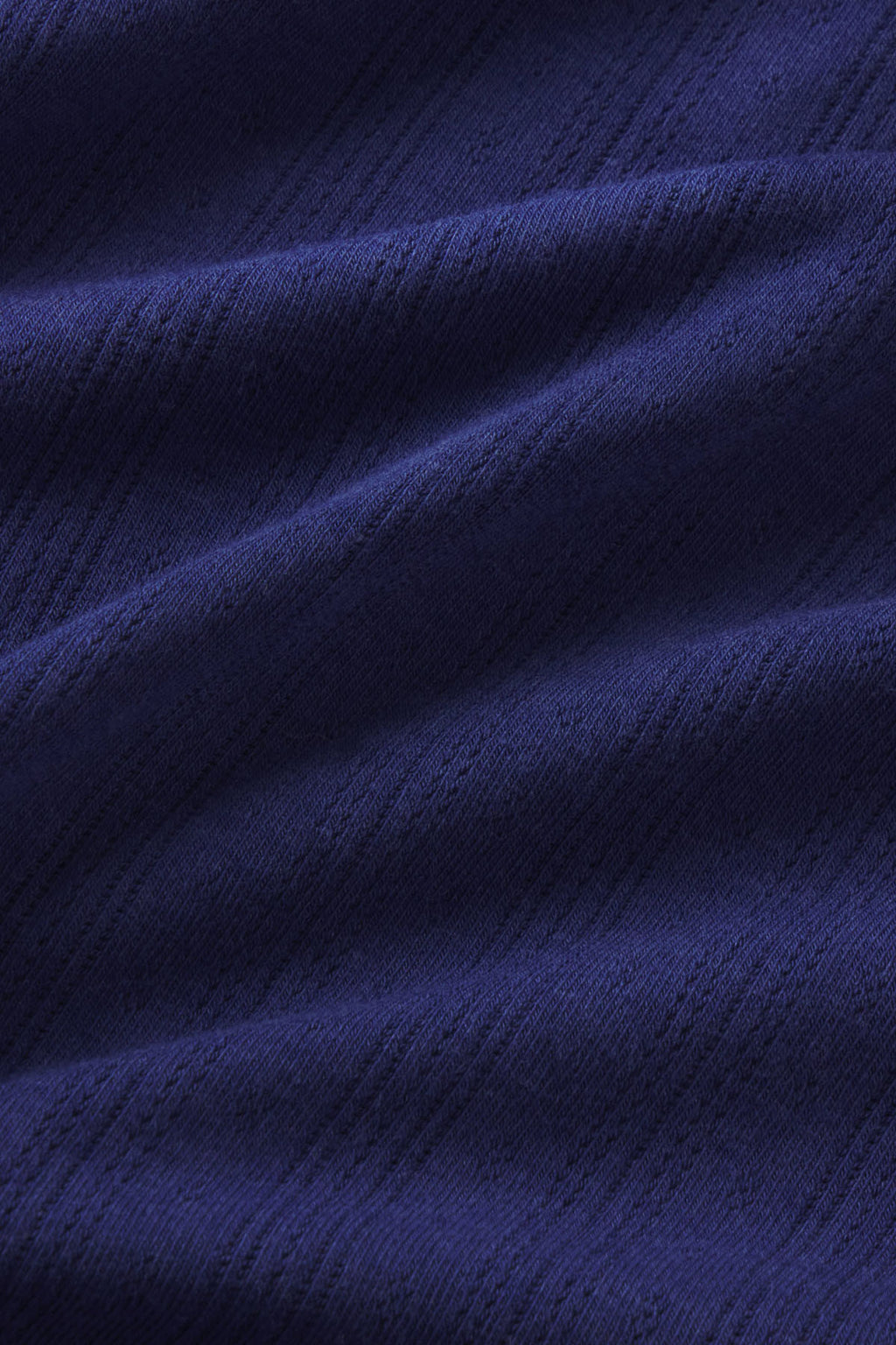 Close-up of dark blue pointelle knit fabric with textured diagonal ribbing and subtle texture pattern.